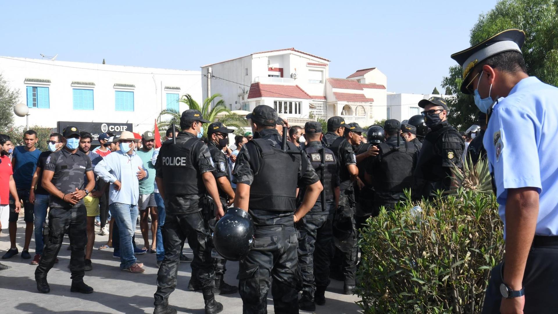 Polizisten in schwarzer Kleidung und Demonstranten stehen auf der Straße.