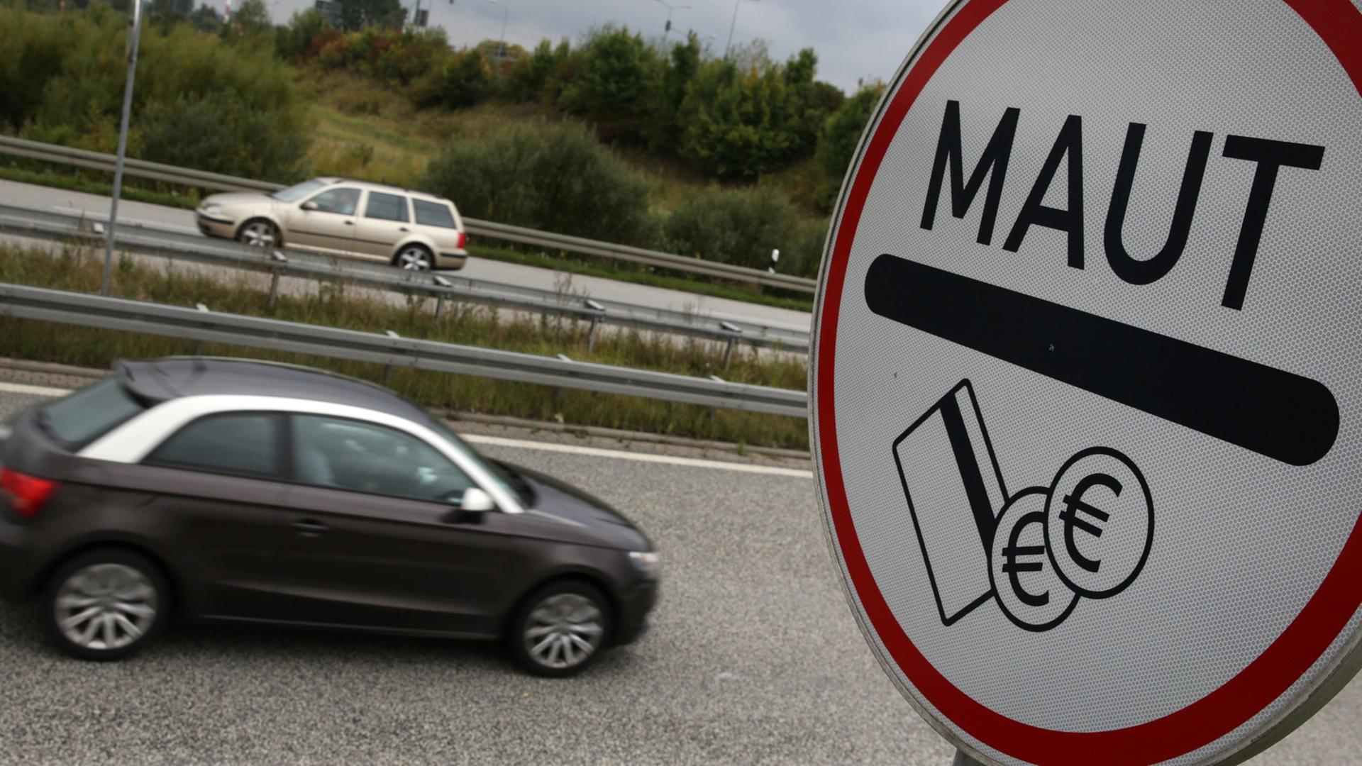 Ein Schild mit der Aufschrift "Maut" steht an einer Autobahn, im Hintergrund fahren Autos vorbei. Ein Schild mit der Aufschrift "Maut" steht an einer Autobahn, im Hintergrund fahren Autos vorbei.