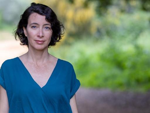 Porträt der Autorin in einem kurzärmeligen, blauen Oberteil unter Bäumen.