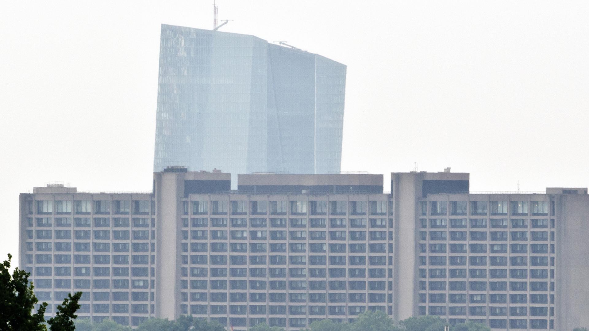 Blick aus der Ferne auf das Gebäude der Bundesbank, hinter dem der Turm der Europäischen Zentralbank hervorragt. Der Himmel ist diesig-weiß.