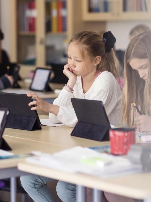 In einem Klassenzimmer sitzen Kinder die an Tablets arbeiten.