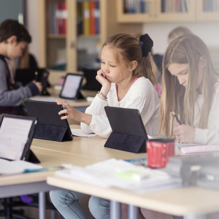 In einem Klassenzimmer sitzen Kinder die an Tablets arbeiten.