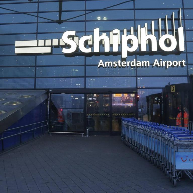 Der Flughafen Schiphol in Amsterdam, zu sehen ist die Außenfassade mit dem Schriftzug Schiphol in der Abenddämmerung.