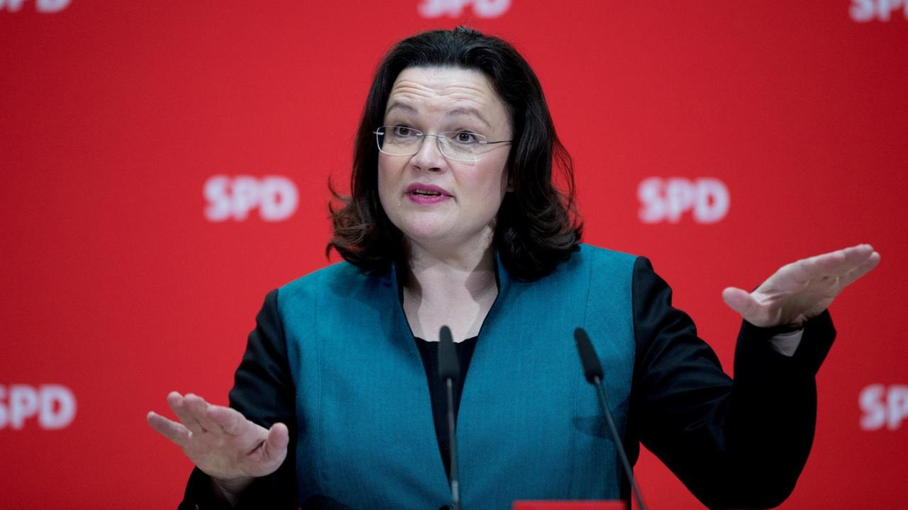 Bundesarbeitsministerin Andrea Nahles gestikuliert vor einer roten Wand mit SPD-Logos.