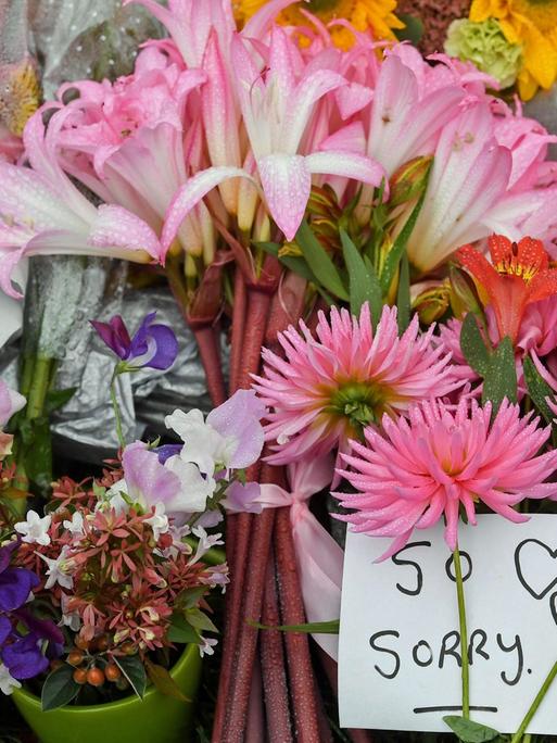 Zwischen Blumen liegt am 17.3.2019 in Christchurch ein Zettel auf dem "So Sorry" steht.