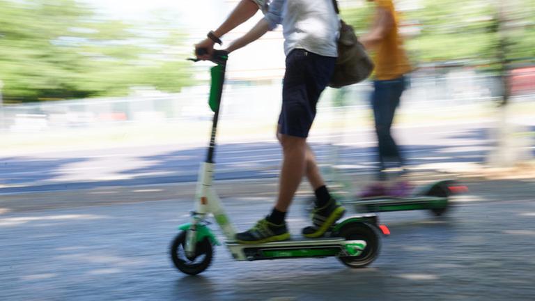 Zwei Personen fahren mit Elektrorollern auf einem Radweg und Pflastersteinen Zwei Personen fahren mit Elektrorollern auf einem Radweg und Pflastersteinen
