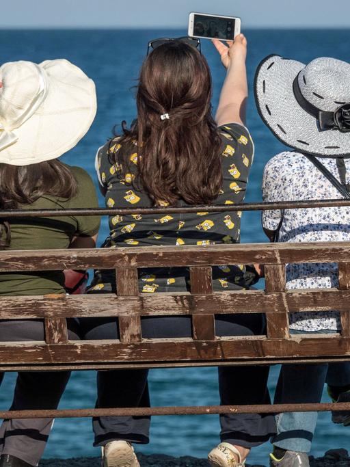 Drei Touristinnen sitzen in Antalya auf einer Bank und blicken aufs Meer.