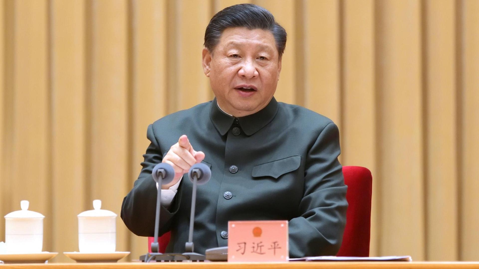 Chinas Staats- und Parteichef Xi Jinping sitzt vor zwei Mikrofonen.