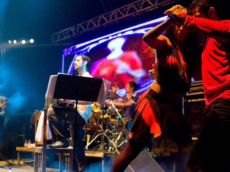 Die spanisch-argentinische Band Otros Aires ist bei einem Auftritt 2010 in Brasilien auf der Bühne zu sehen. Im Vordergrund tanzt ein Paar Tango.