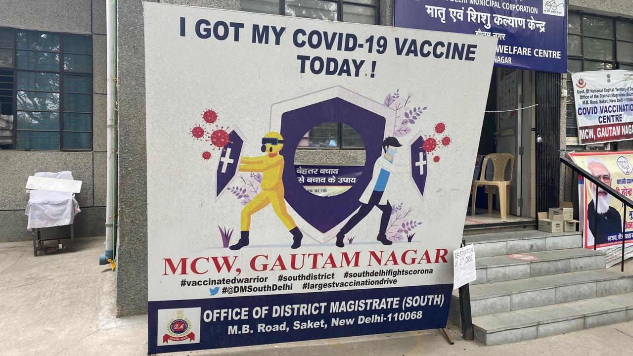 Vor einem Hauseingang steht ein großes Plakat, auf dem bunte Männchen mit Schildern das Coronavirus abwehren.