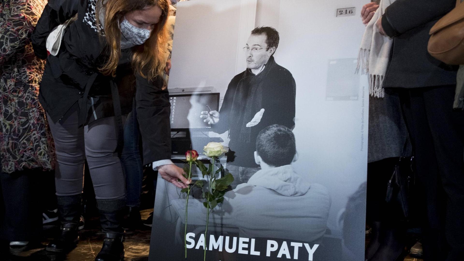 Ein Foto des Lehrers Samuel Paty, eine Frau lehnt eine Rose daran.