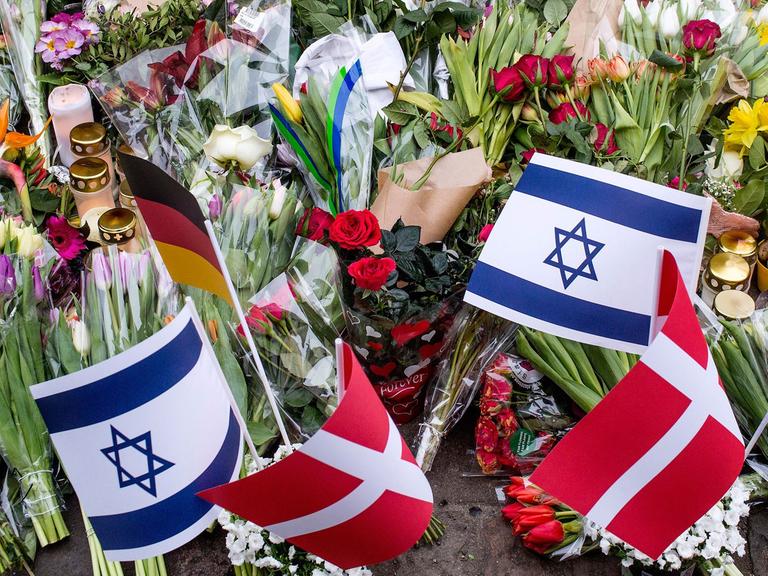 Vor der jüdischen Synagoge in Kopenhagen liegen nach dem Anschlag tausende Blumen; einige Menschen haben auch kleine Fahnen von Israel, Dänemark und Deutschland in das Blumenmeer gesteckt.