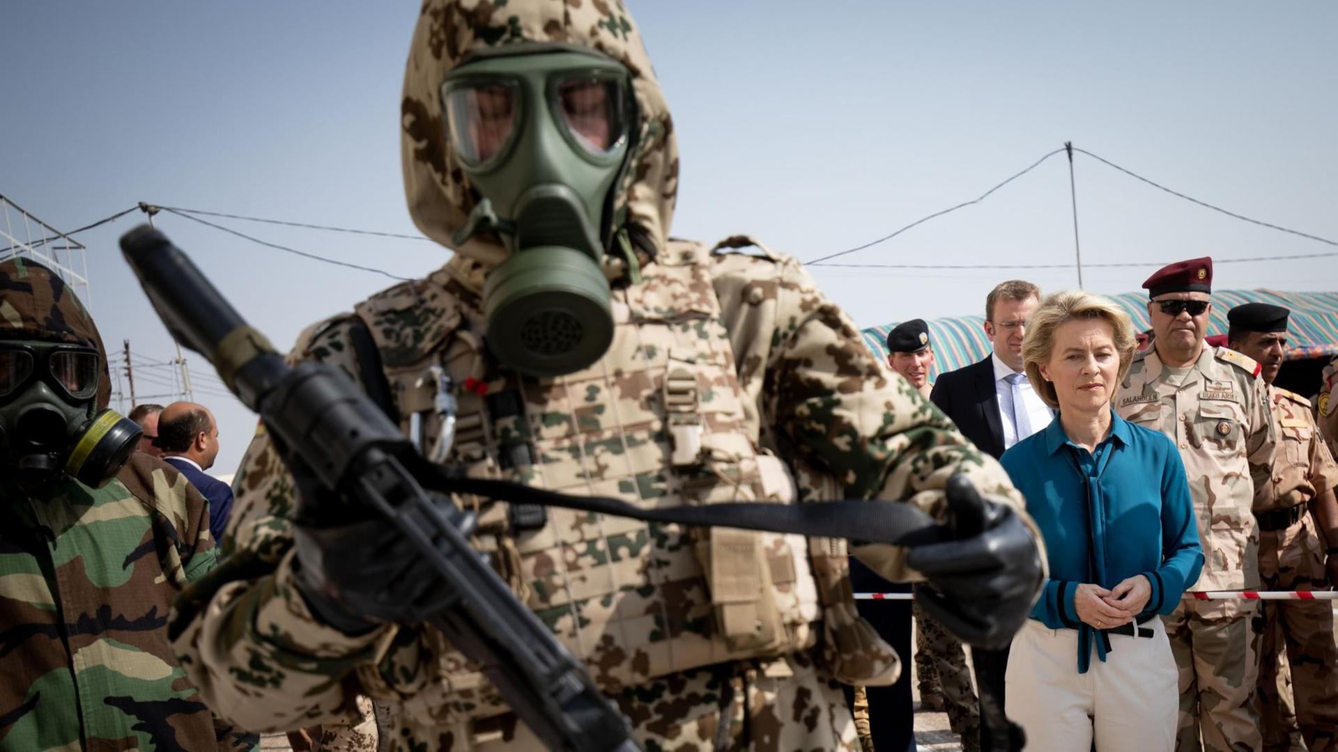 Bundesverteidigungsministerin Ursula von der Leyen steht beim Besuch im irakischen Armeestützpunkt Tadschi zwischen Bundeswehrsoldaten im Kampfanzug. Der Soldat im Vordergrund trägt eine Gasmaske.
