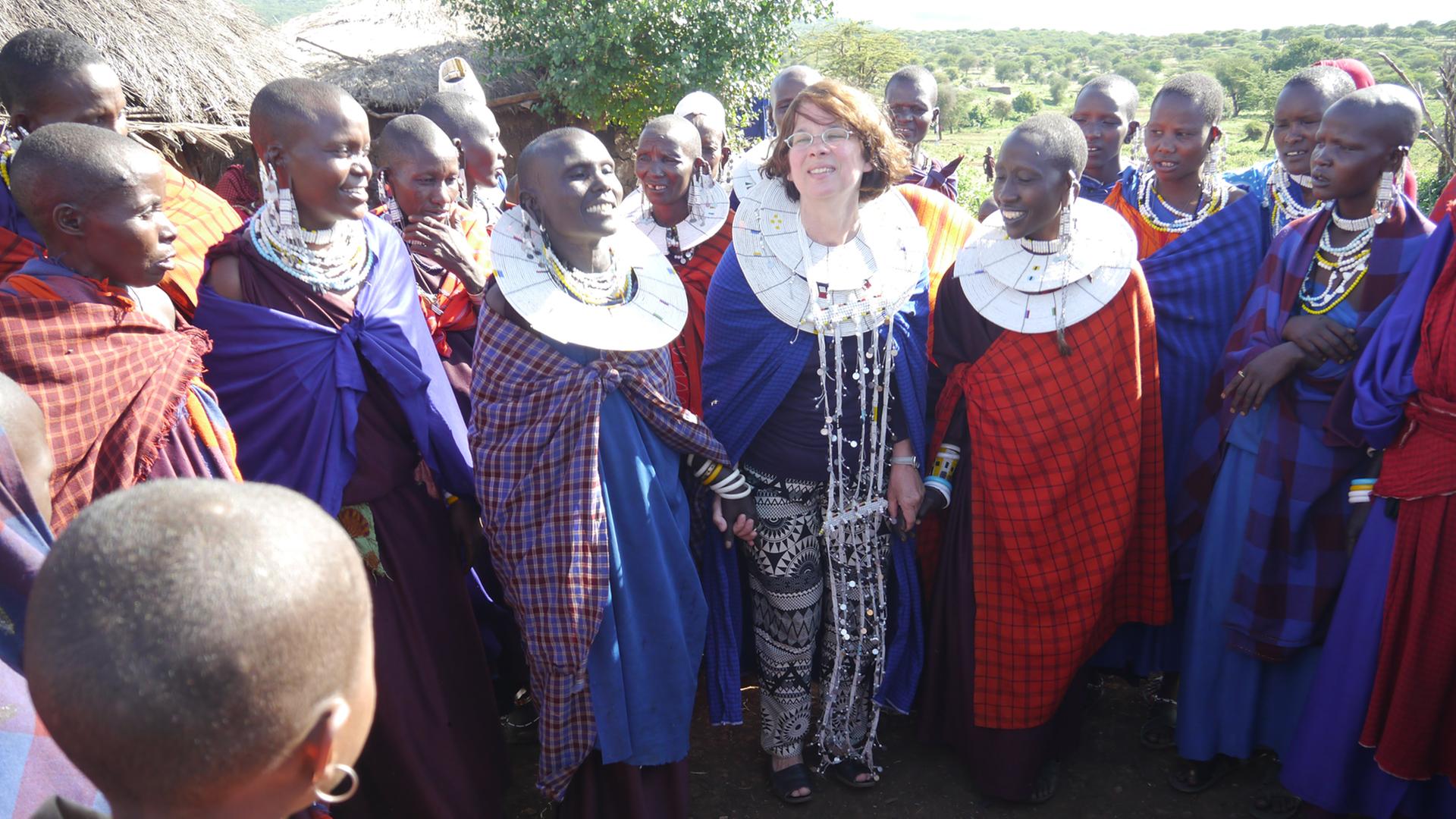 Die Autorin Bettina Brand (Mitte) steht in Tansania zwischen Einheimischen Frauen.
