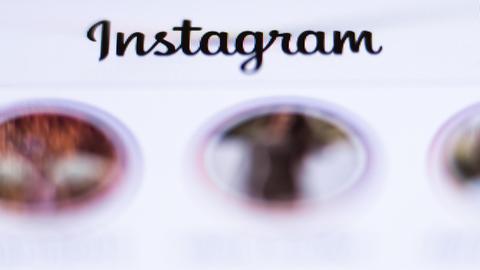 Der Schriftzug «Instagram» ist über der geöffneten App des Fotonetzwerks auf einem Display eines Smartphones zu sehen.