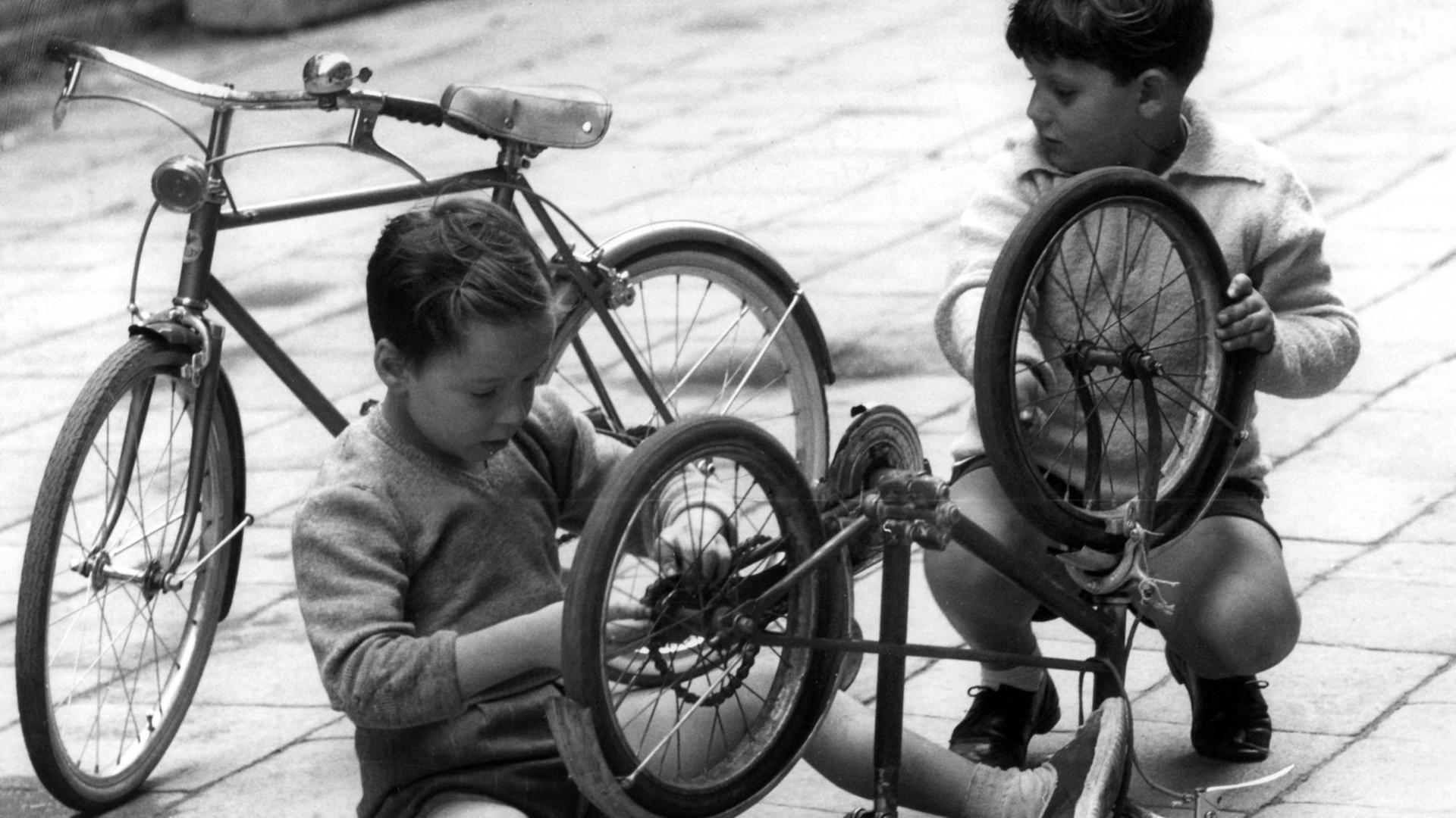 Zwei Kinder in Venedig brauchen nicht bei jeder Kleinigkeit in ein Fachgeschäft zu gehen. Sie reparieren kleinere Macken an ihren Drahteseln einfach selbst. Aufnahme vom 27.09.1960