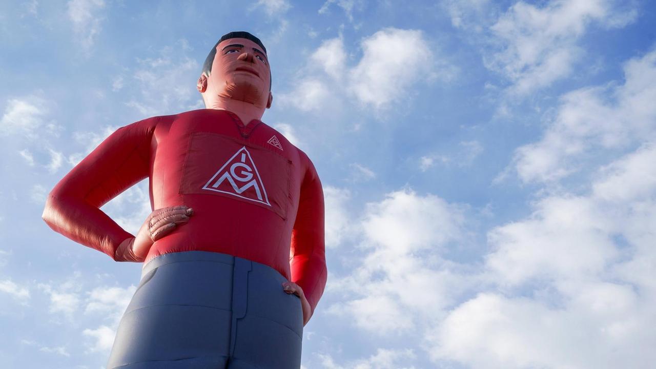 Eine große aufgeblasene Puppe mit IGM-Logo auf der Brust vor blauem Himmel