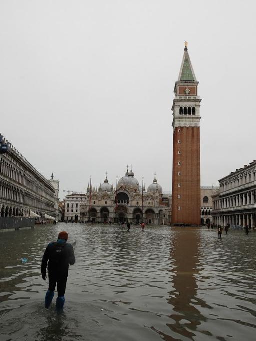 Das Bild zeigt einen Mann, der den überfluteten Markusplatz in Venedig überquert.