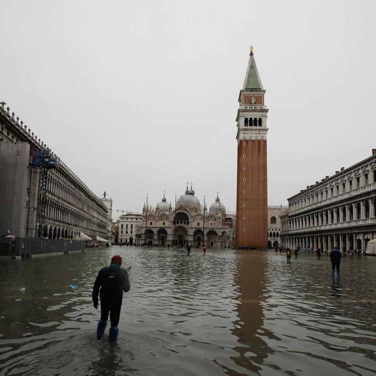 Das Bild zeigt einen Mann, der den überfluteten Markusplatz in Venedig überquert.