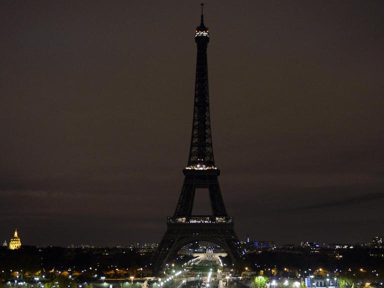 Man sieht den Eiffelturm aus einiger Entfernung in der Nacht. Straßenlaternen leuchten.