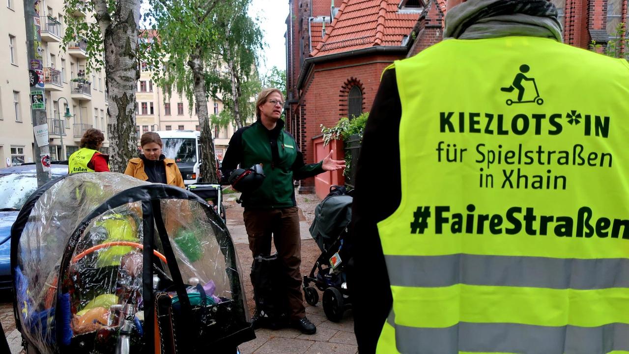 Amtsleiter Felix Weisbrich steht mit mehreren Menschen auf einer Straße. Eine Person trägt eine Warnweste mit der Aufschrift "Kiezlots*in für Spielstraßen in Xhain - #FaireStraßen."