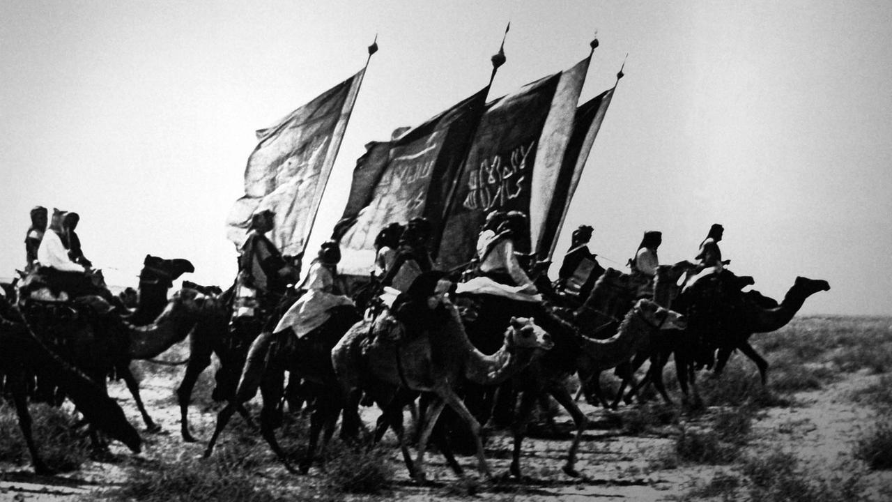 Wahhabitische Kämpfer auf Kamelen Anfang des 19. Jahrhunderts auf einem schwarz-weißen, historischen Foto.