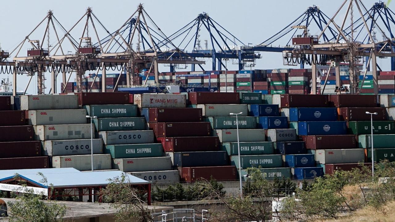 Container stapeln sich vor Verladekränen im Hafen von Piräus, Griechenland. Der Hafen ist mehrheitlich im Besitz von China Ocean Shipping Company (COSCO), der drittgrößten Containerschiff-Reedereien der Welt. Das Unternehmen ist ein volkseigener Betrieb der Volksrepublik China mit Sitz in Peking. Im Oktober 2009 mietete Griechenland die Docks 2 und 3 von PPA für einen Zeitraum von 35 Jahren an COSCO . Für seine Präsenz im Hafen zahlt COSCO jedes Jahr 100 Millionen Euro.