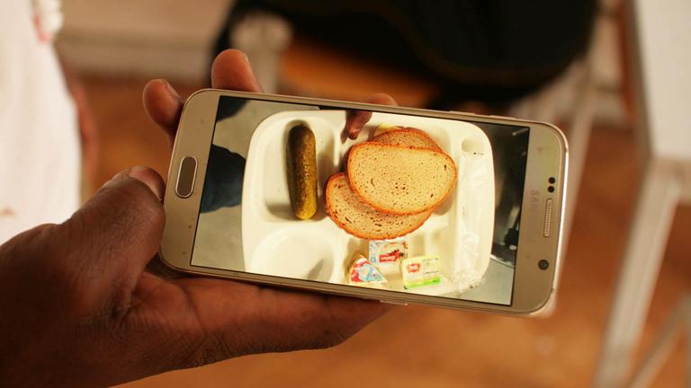 Zwei Scheiben Brot, ein bisschen Butter: das Abendessen in der Unterkunft - Arona zeigt ein Bild von der Mahlzeit auf seinem Handy.