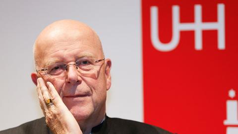 Der Präsident der Universität Hamburg, Dieter Lenzen, im Porträt. Er stützt eine Hand im Gesicht auf, im Hintergrund ist ein rotes Plakat zu sehen.