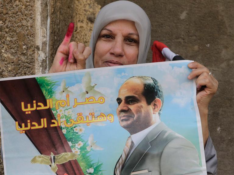 Eine Ägypterin nach der Wahl zeigt ihren mit Farbe markierten Finger, in der Hand ein Plakat mit Abdel Fattah al-Sissi.