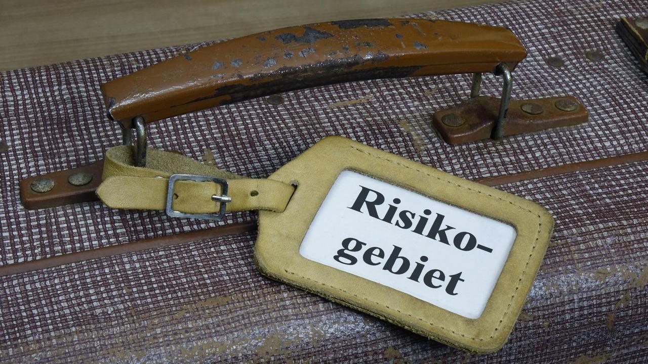 Auf einem Koffergriff ist ein Schild mit dem Wort "Risikogebiet" befestigt.