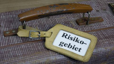 Auf einem Koffergriff ist ein Schild mit dem Wort "Risikogebiet" befestigt.