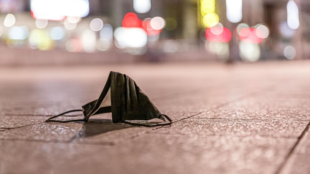 Eine schwarze Mund-Nasen-Bedeckung liegt auf dem Boden in einer Fußgängerzone bei Nacht. 