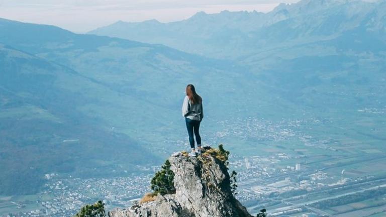 Eine junge Frau steht in Liechtenstein auf dem Fürstensteig und blickt auf die Landschaft unter ihr.