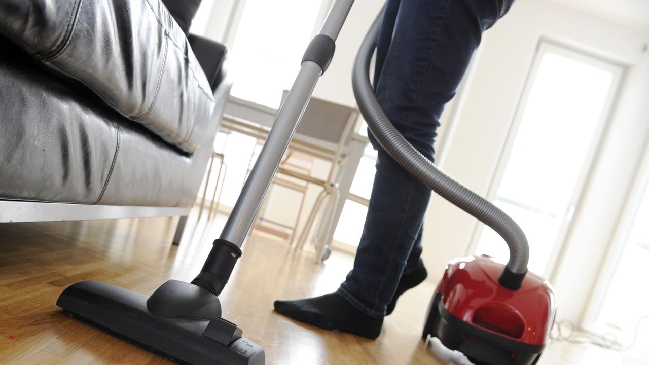 Eine Frau saugt mit einem Staubsauger den Fußboden eines Wohnzimmers.