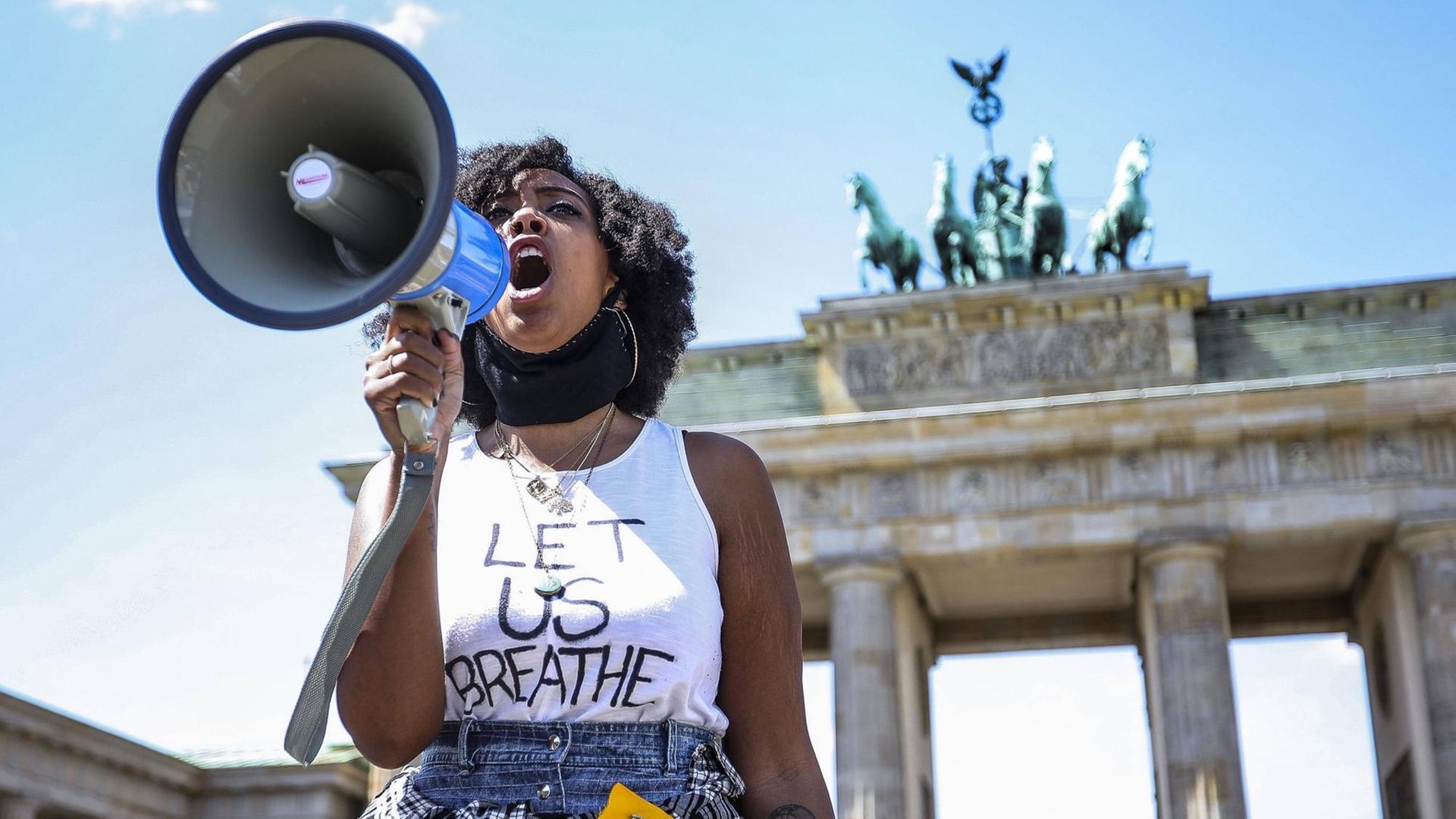 Eine Frau steht vor dem Brandenburger Tor, sie ruft in ein Megafon.