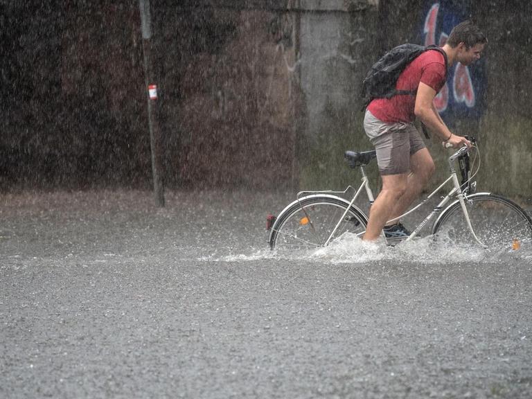 Ein Fahrradfahrer fährt auf einer überfluteten Straße in Köln im Wasser mit ihrem Rad.