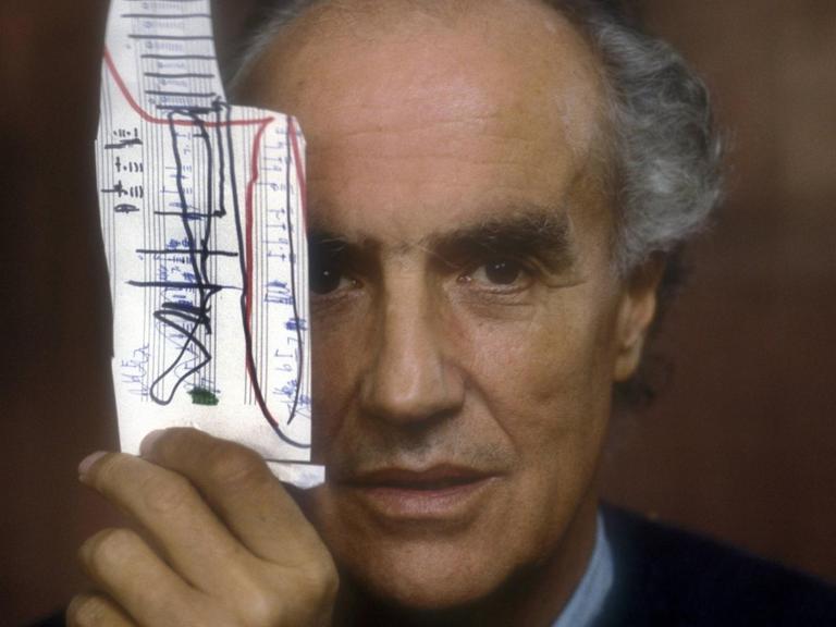 Das Foto zeigt in Frontalansicht den italienischen Komponisten Luigi Nono. Er hält sich ein Stück Notenpapiert vor sein rechtes Auge. Das Foto entstand 1988.