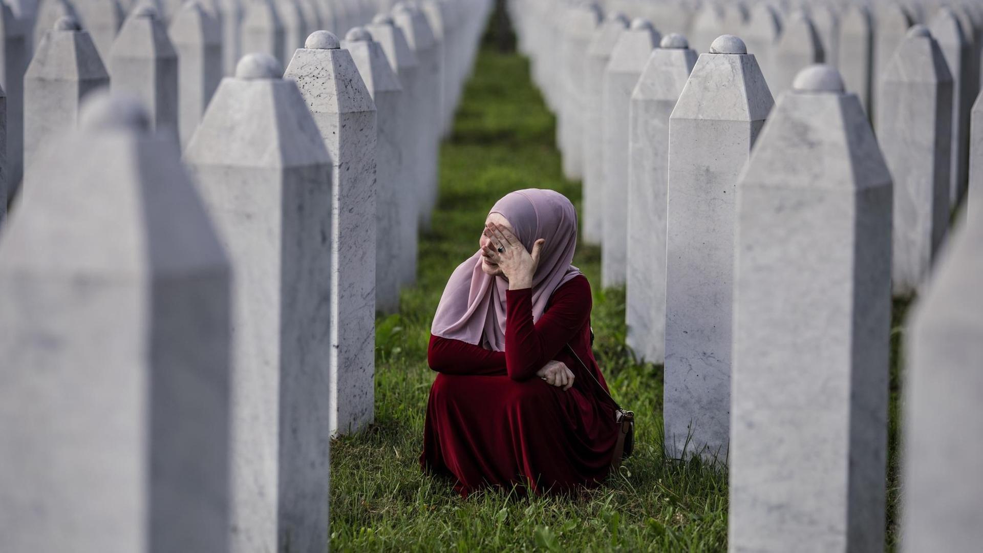 Eine bosnisch-muslimische Frau weint zwischen den Gräbern ihres Vaters, zweier Großväter und anderer enger Verwandter, auf dem Friedhof in Potocari in der Nähe von Srebrenica, Bosnien und Herzegowina.