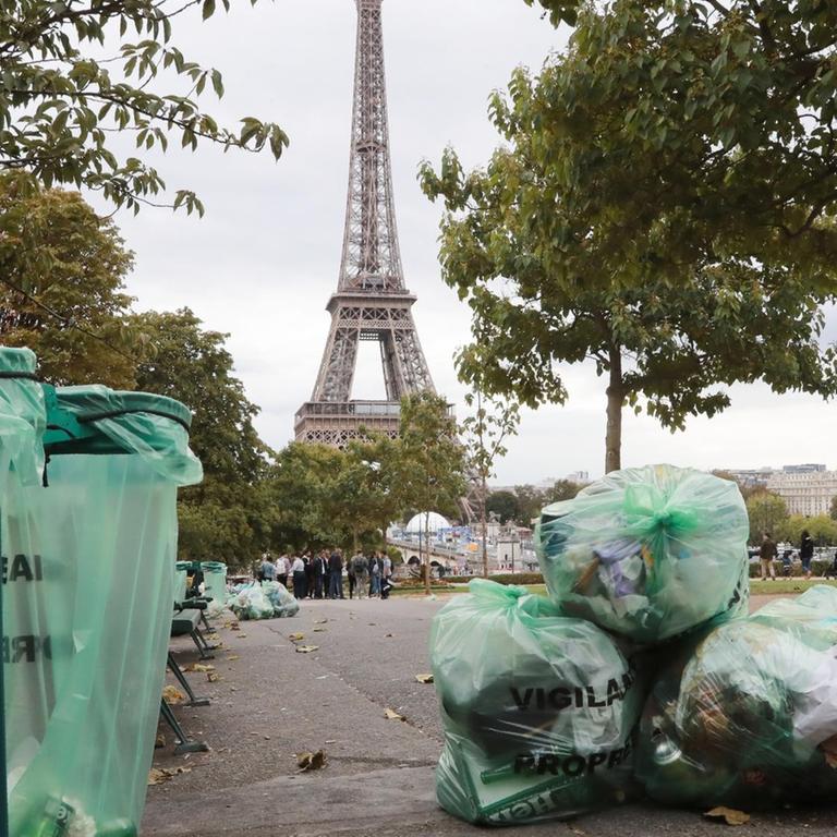 Plastiktüten mit Müll liegen neben Mülltonnen in einer Pariser Straße mit dem Eiffelturm im Hintergrund.