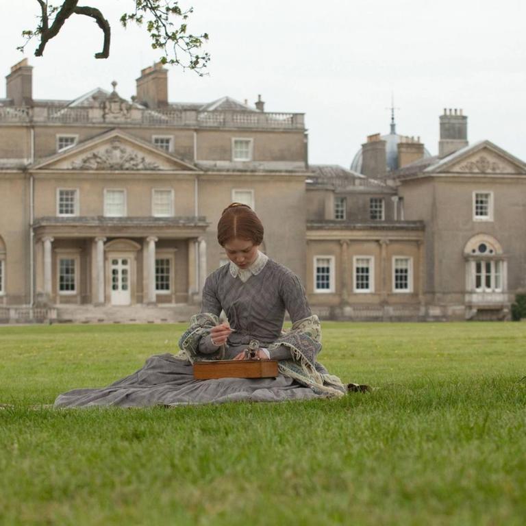 Eine Frau sitzt auf einer großen Rasenfläche vor einem großen Landhaus in England