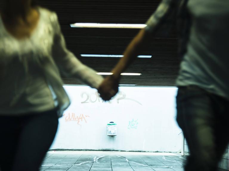 Zwei Jugendliche laufen Hand in Hand durch eine Unterführung
