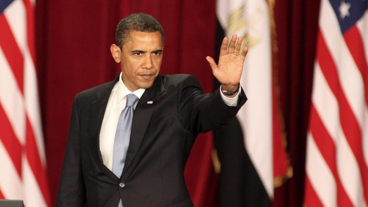 Obama streckt begrüßend seinen Arm in die Luft. Im Hintergrund sind USA-Fraggen und die ägyptische Flagge zu sehen.