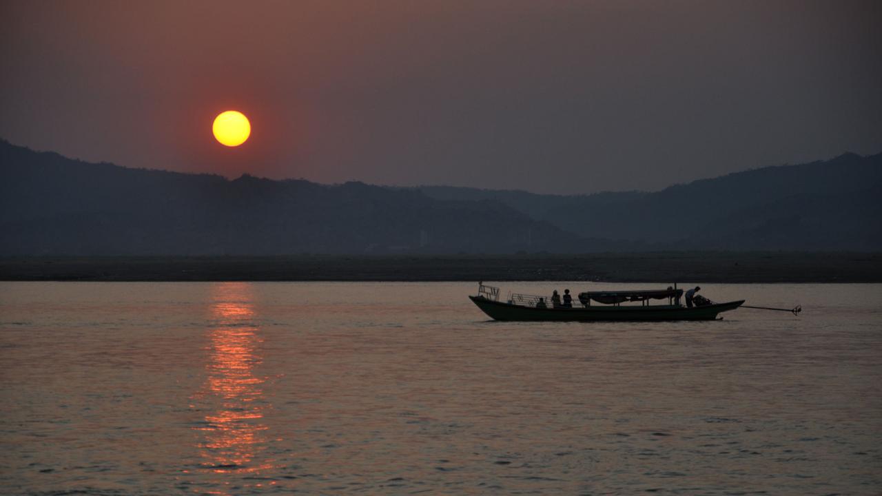 Die Sonne geht über dem burmesischen Fluss Irrawaddy in Myanmar. Ein Boot fährt auf dem Wasser.