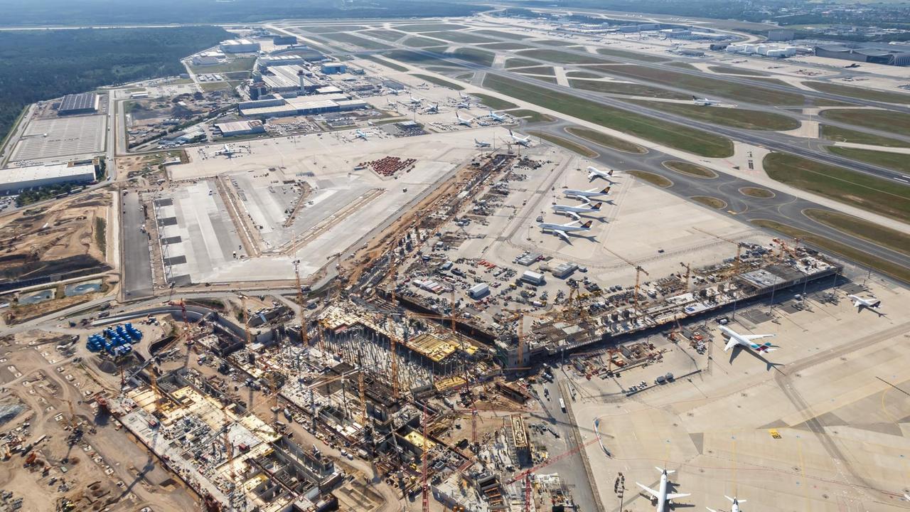 Luftbild. Im Vordergrund die Baustelle des neuen Terminals, im Hintergrund Start- und Landebahn des Flughafens.