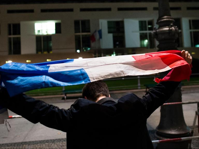 Ein Mann hält am 14.11.2015 vor der Französischen Botschaft in Berlin, die Flagge Frankreichs über seinen Kopf. Bei den Angriffen .