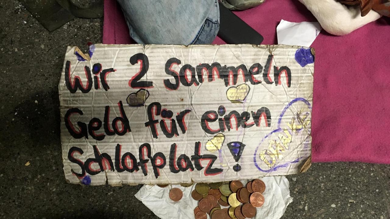 Ein Sammelbecher mit etwas Kleingeld, dazu ein Schild: "Wir zwei sammeln für einen Schlafplatz"