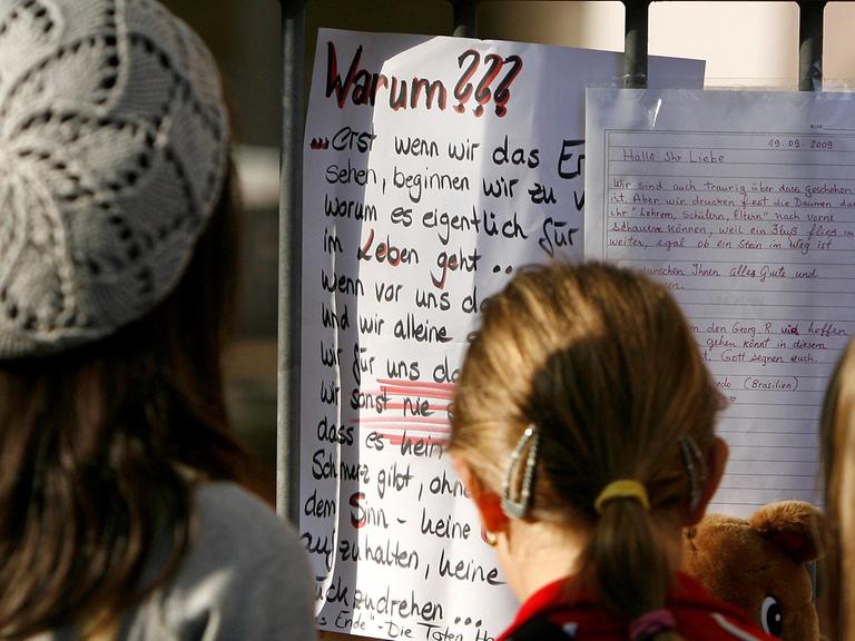 Jugendliche betrachten an einem Schultor einen Zettel mit dem Titel "Warum???"