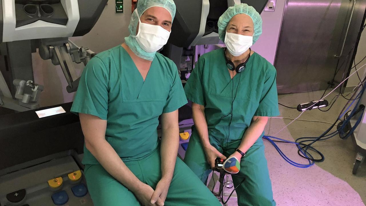 Deutschlandradio-Korrespondentin Anke Petermann (r.) mit dem Chirurgen Werner Kneist im Operationssaal vor dem "Da Vinci"-Roboter