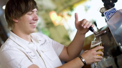 Junger Kellner zapft ein Bier an einer Zapfanlage.